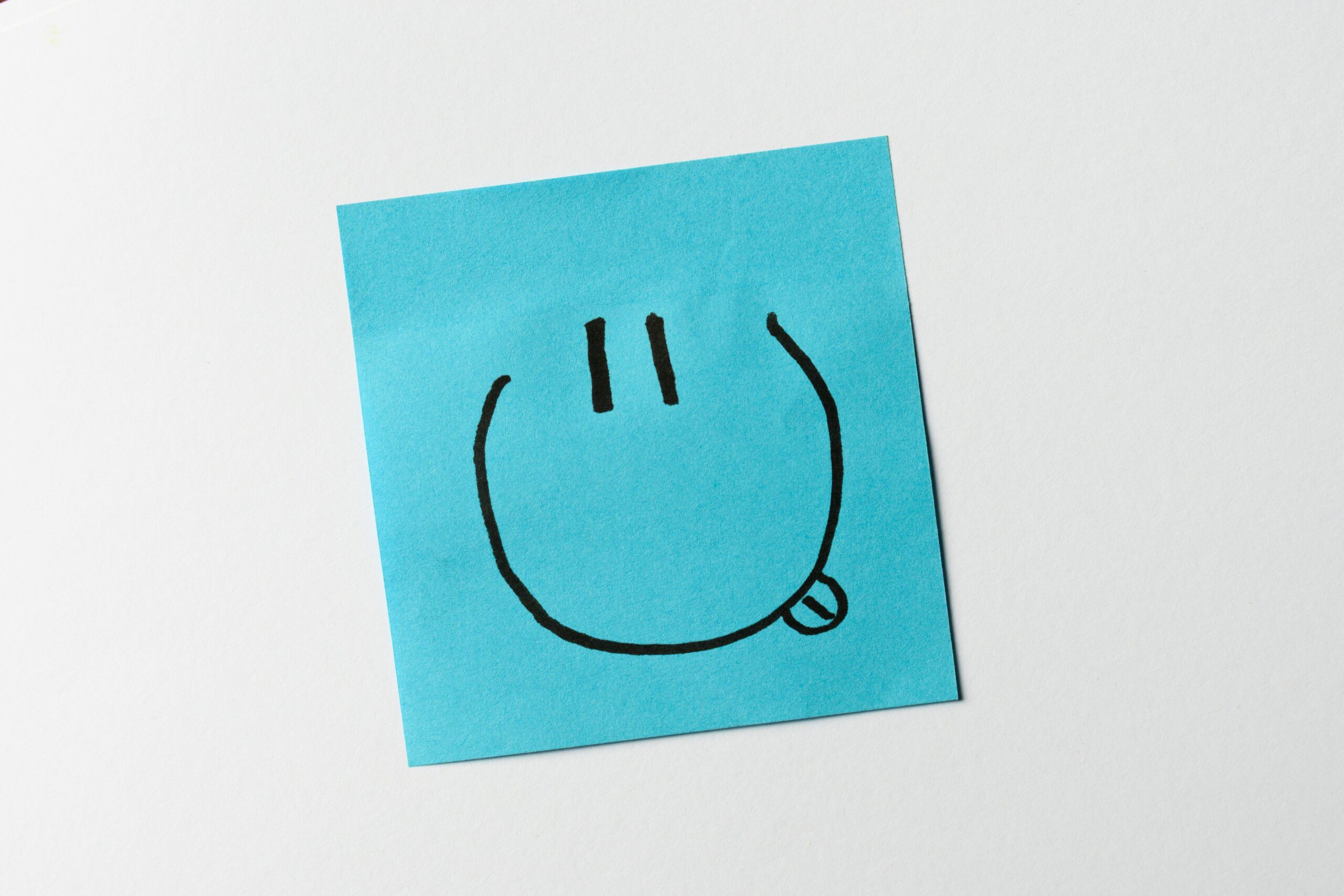 A blue sticky note featuring a simple hand-drawn smiling face with a tongue out expression.