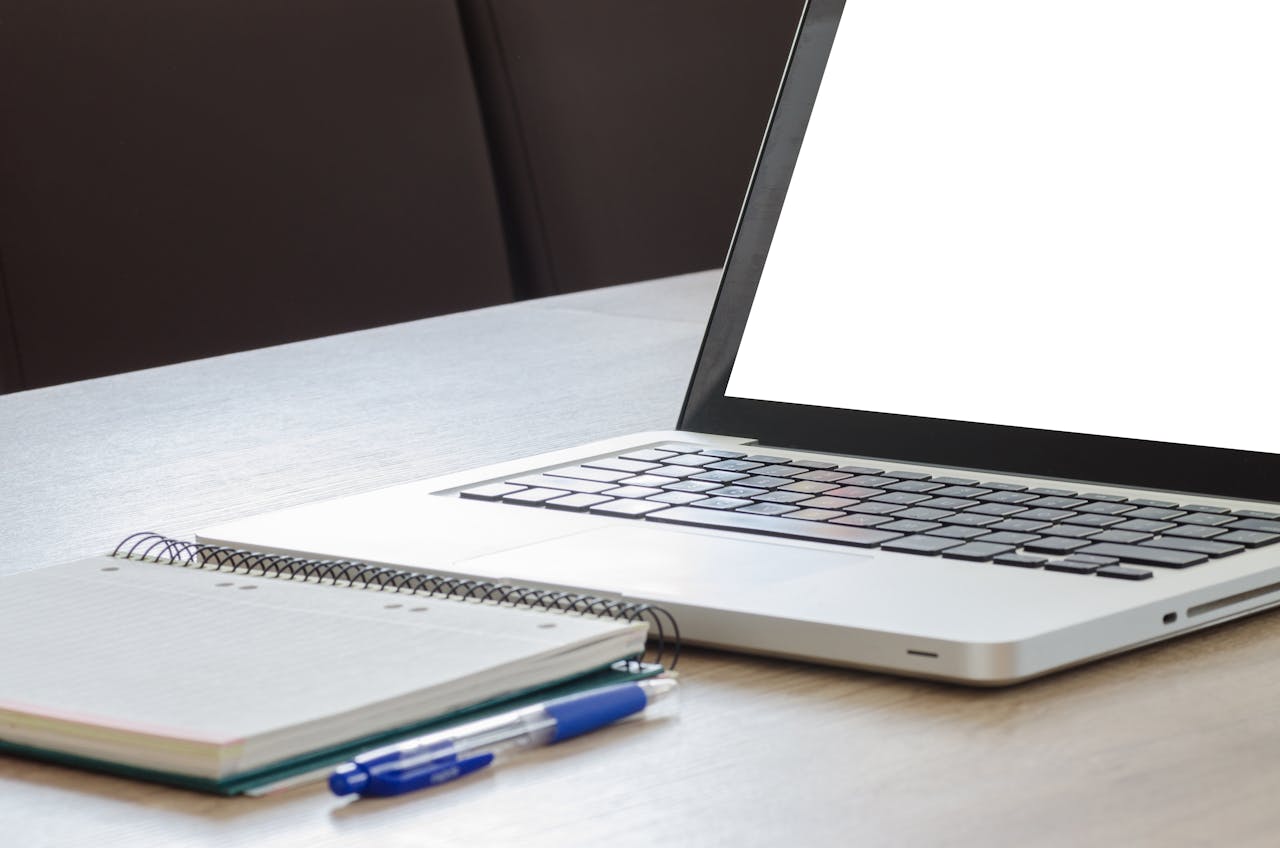 Home Open laptop with blank screen, notebook, and pen on a wooden desk, ideal for work or study.